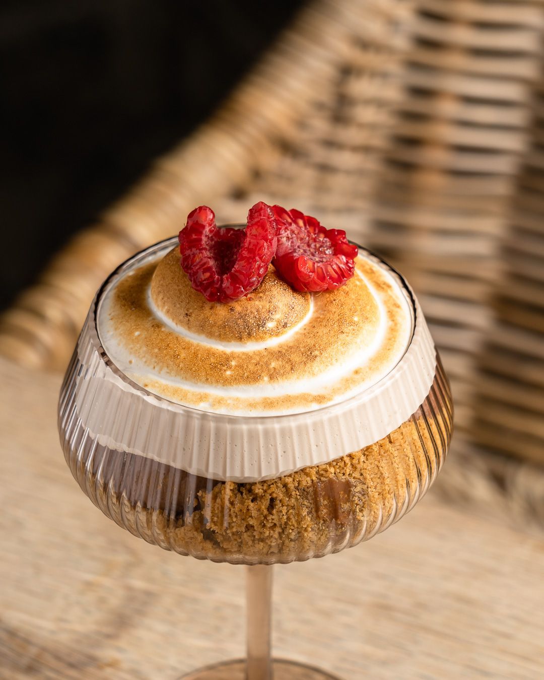 Dessert in a stemmed glass with layers of crumbled crust, chocolate, toasted meringue, and raspberries.