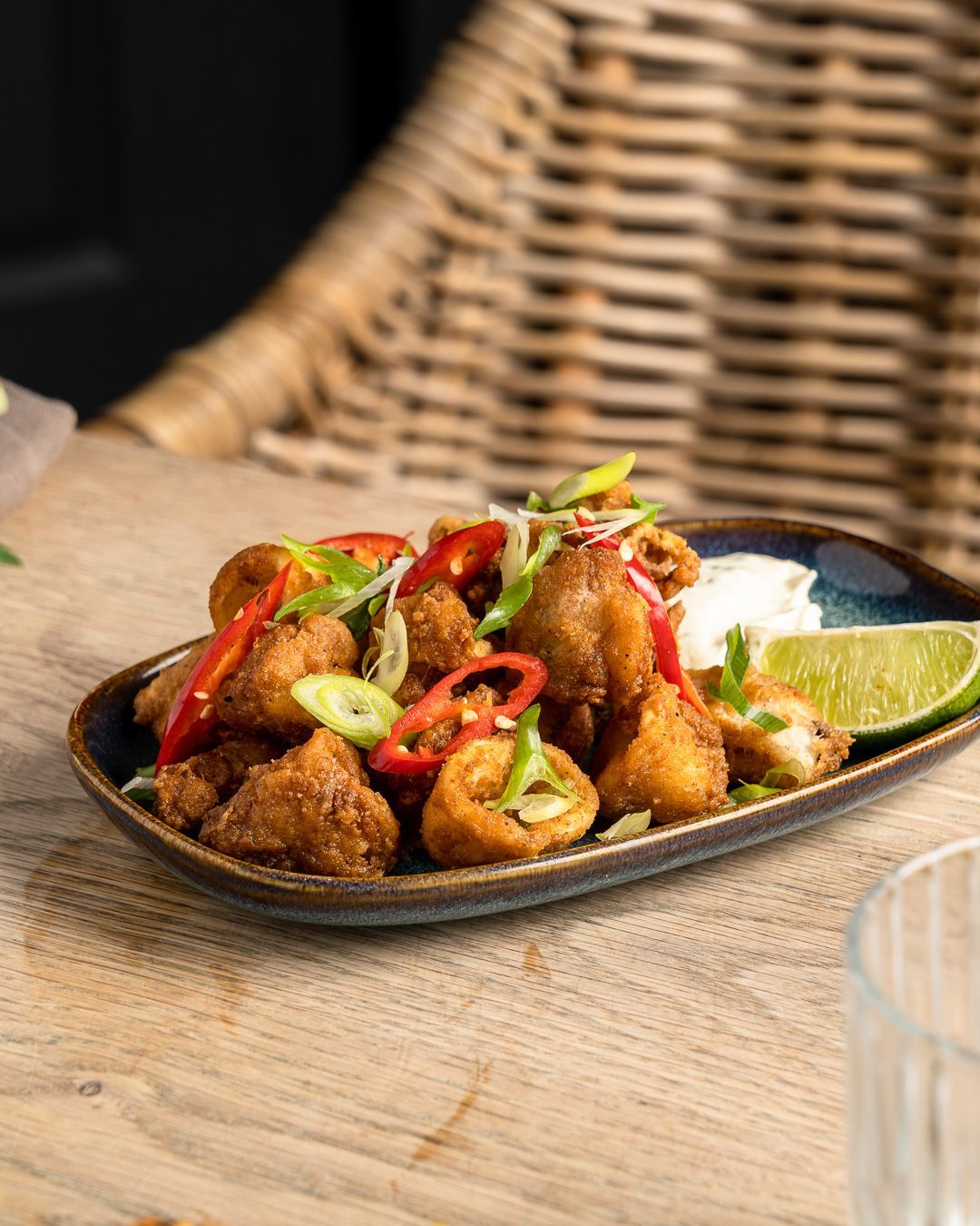 Fried food with red chili slices, scallions, lime, and dipping sauce on a rectangular plate.