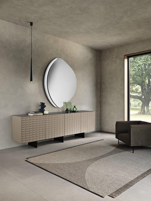 Soggiorno minimalista con credenza bassa, specchio rotondo a parete, lampada a sospensione e ampia finestra.