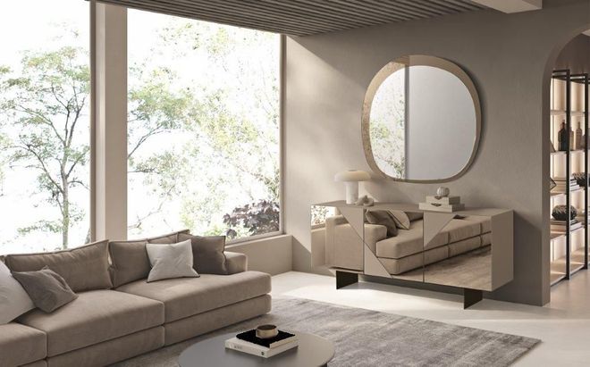 Soggiorno minimalista sui toni del beige con ampie finestre, divano componibile, specchio rotondo e chaise longue.