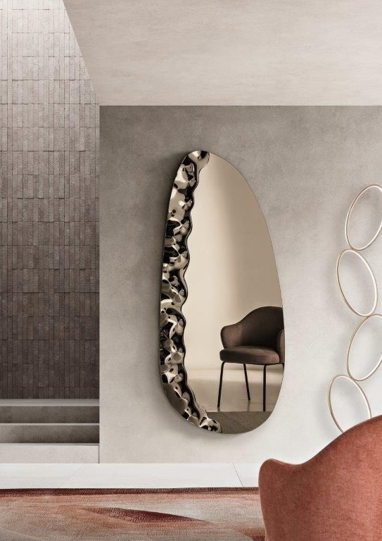 Interno moderno con specchio ovale, parete grigia, sedia marrone e decorazioni con texture.