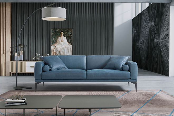 Soggiorno moderno con divano blu, tappeto grigio, lampada da terra e ritratto incorniciato su tende scure.