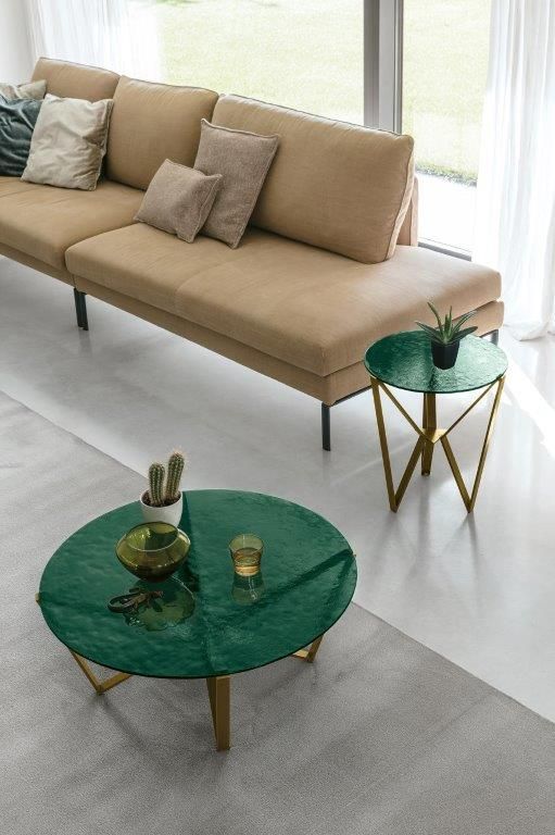Soggiorno moderno con divano beige e tavolini rotondi verdi su un tappeto chiaro e pavimento bianco.