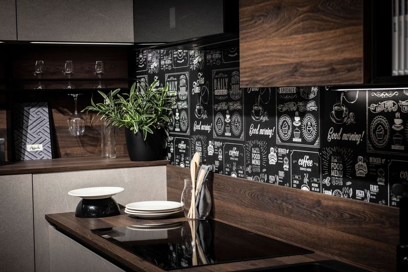 Cucina moderna con mobili scuri, paraschizzi decorato e bancone per la colazione con piatti e un vaso di piante.