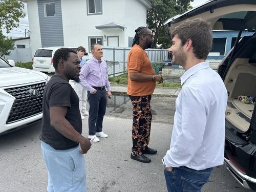 Four people stand talking beside an open SUV trunk on a suburban street.
