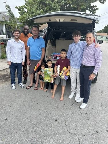 Family standing behind an open SUV trunk on a street, with two children in front holding items.