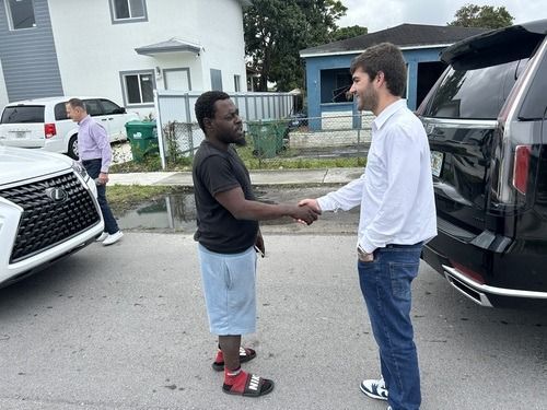 Two men shaking hands beside a black SUV in a residential driveway