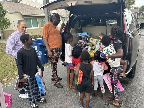 People loading colorful donated items into an SUV in a neighborhood driveway