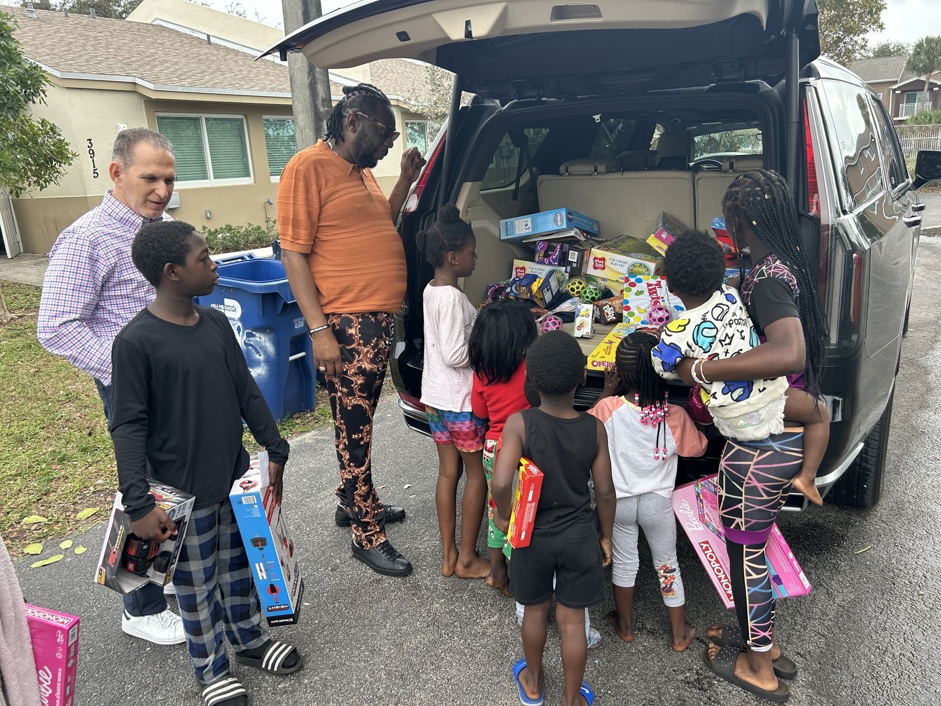 People unloading colorful bags and toys from an open SUV in a driveway
