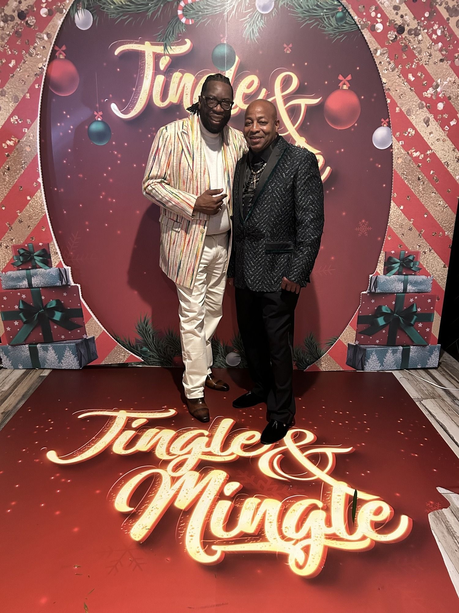 Two men posing on a festive Jingle & Mingle holiday backdrop with pink and red decor