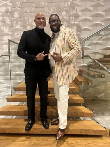 Two men posing on stairs, smiling and standing arm in arm in a modern lobby.