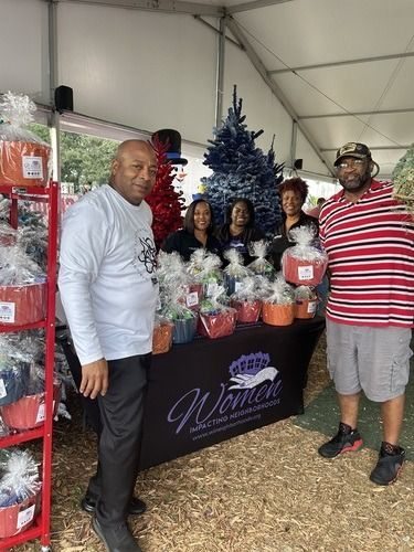 Five people posing at a holiday market booth with decorated gift baskets and Christmas trees.