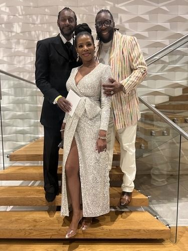 Three people posing on a staircase, dressed in formal attire, smiling indoors.