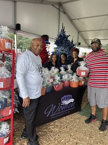 People posing at a holiday gift display under a tent, with wrapped baskets and a decorated Christmas tree.
