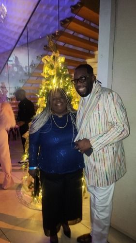 Two people posing indoors beside a lit decorative tree at an event