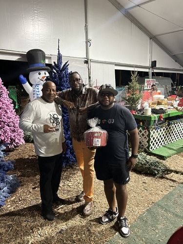 Three people posing with gift baskets at a holiday display under a tent