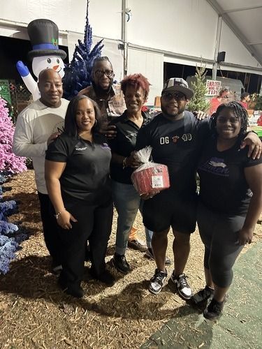 Group posing outdoors at a festive display with a large snowman and pink decorations, smiling for a photo.