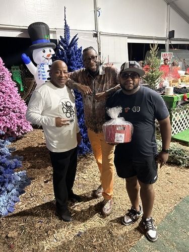 Three people posing outdoors beside colorful holiday decorations and a snowman.