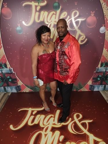Couple posing in front of a festive “Jingle & Mingle” holiday backdrop in red outfits.