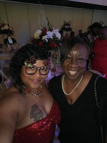 Two people smiling and posing together at an indoor event, one in a red dress and one in a black dress.