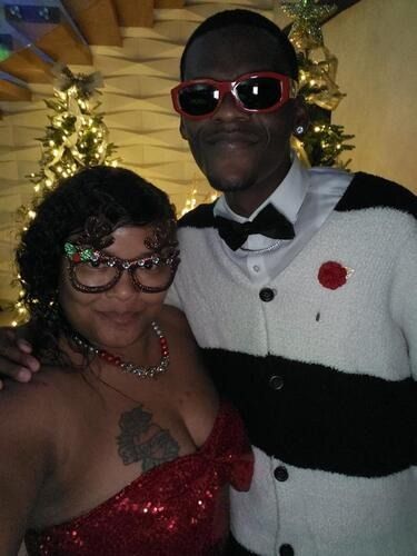 Two people posing indoors in formal attire with festive decorations in the background