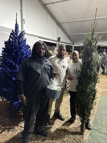 Three people posing between decorated Christmas trees in a tented indoor display.