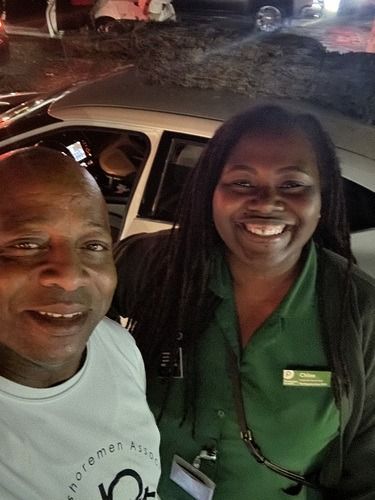 Two smiling people posing outdoors at night, with a white car behind them.