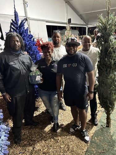 Group posing outdoors at night beside decorated Christmas trees, smiling at the camera.