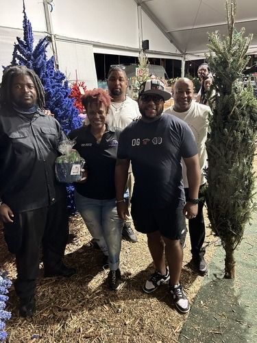 Four people posing outdoors between blue and green trees at a nighttime event.