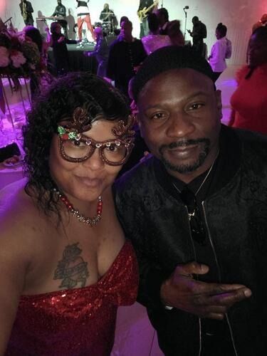 Two people posing at a purple-lit party, smiling and holding up peace signs.