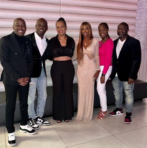 Six people posing together at an event, dressed in black, pink, and gold outfits.