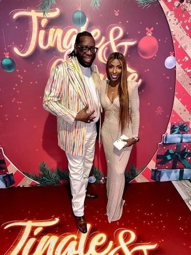 Two people posing on a red carpet before a pink “Tina &” backdrop with balloons and gift boxes