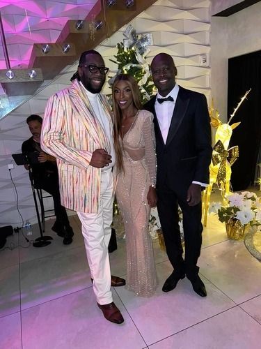 Three people posing in formal attire at an indoor celebration with floral decor.
