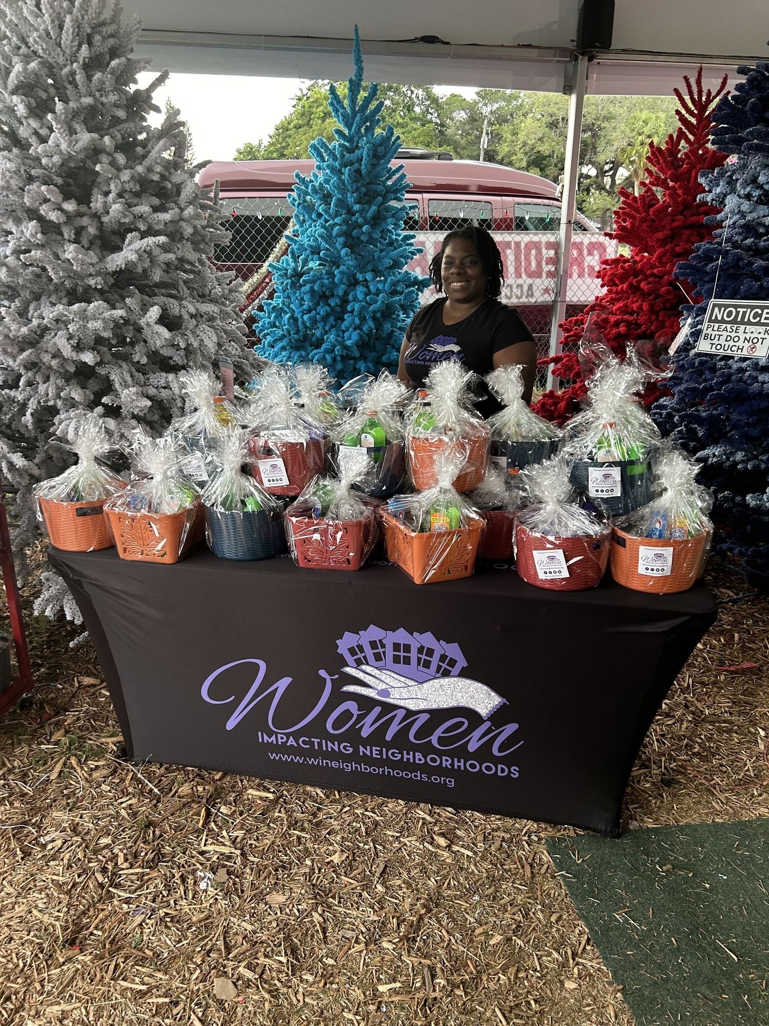 Outdoor market table with decorated mini Christmas trees and gift items under a canopy