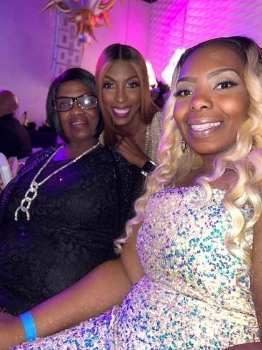 Three people smiling at a party, with pink lighting and sparkly outfits.