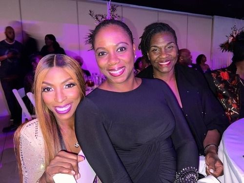 Three smiling people posing together at a purple-lit indoor event