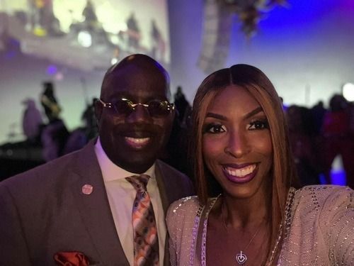 Two people smiling at a formal event, with colorful lights in the background.