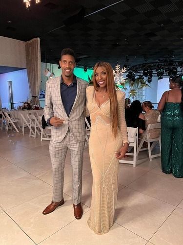 Two people posing together at an indoor event, wearing formal outfits and smiling.