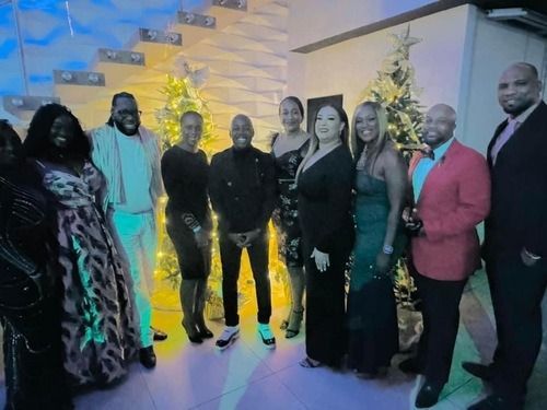 Group of people posing indoors at an event, with blue and yellow lights and decorative steps in the background.