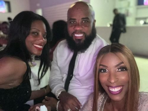 Three smiling people pose together at a dimly lit event table.