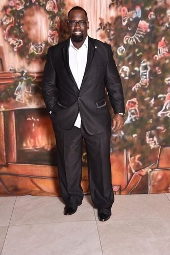 Man in a black suit and white shirt posing in front of a floral mural backdrop