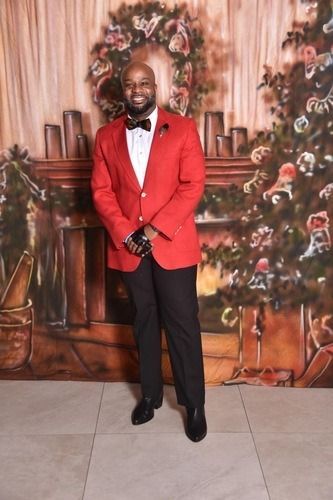 Man in a red blazer posing in front of a floral event backdrop