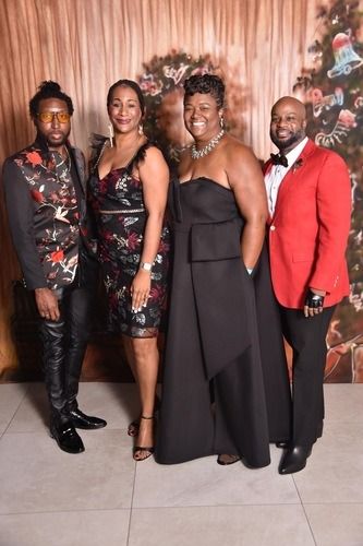 Four people dressed in formal attire pose together at a holiday event in front of a decorated tree.