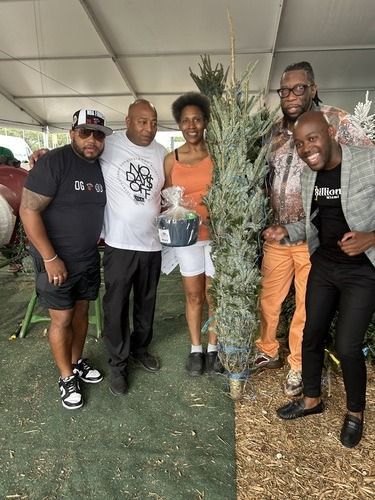 Five people posing under a tent beside a tall, narrow tree display on green flooring.
