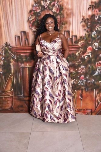 Woman in a floral dress posing in front of a decorative floral backdrop.
