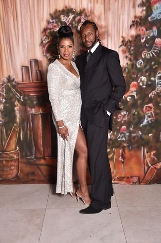 Couple posing on a floral backdrop, with the woman in a silver gown and the man in a black suit.