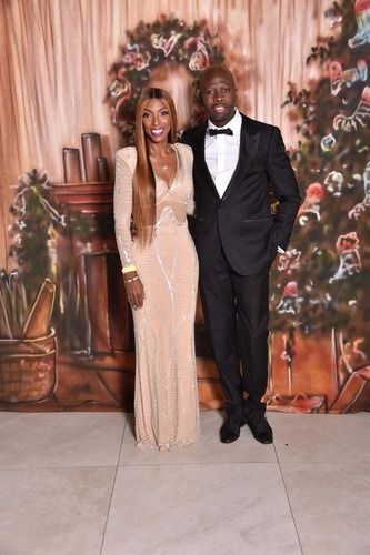 Two people posing in formal attire in front of a floral backdrop
