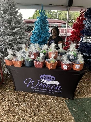 Holiday gift baskets on a Women’s table with decorated Christmas trees and a smiling vendor under a tent
