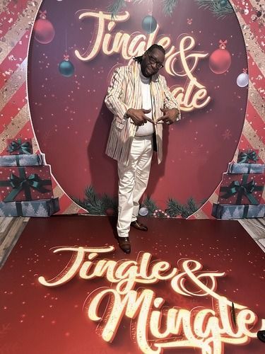 Person posing on red carpet before “Jingle & Mingle” holiday backdrop with gift boxes