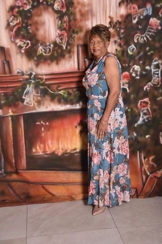 Woman in a blue floral dress posing in front of a painted fireplace backdrop.